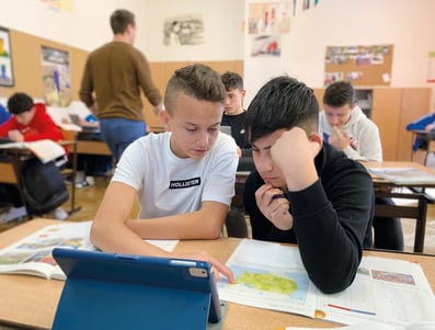In einem gefüllten Klassenzimmer arbeiten zwei Jungs gemeinsam an einer Aufgabe aus Geografie